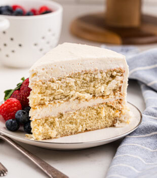 a slice of frosted vanilla layer cake served with fresh berries