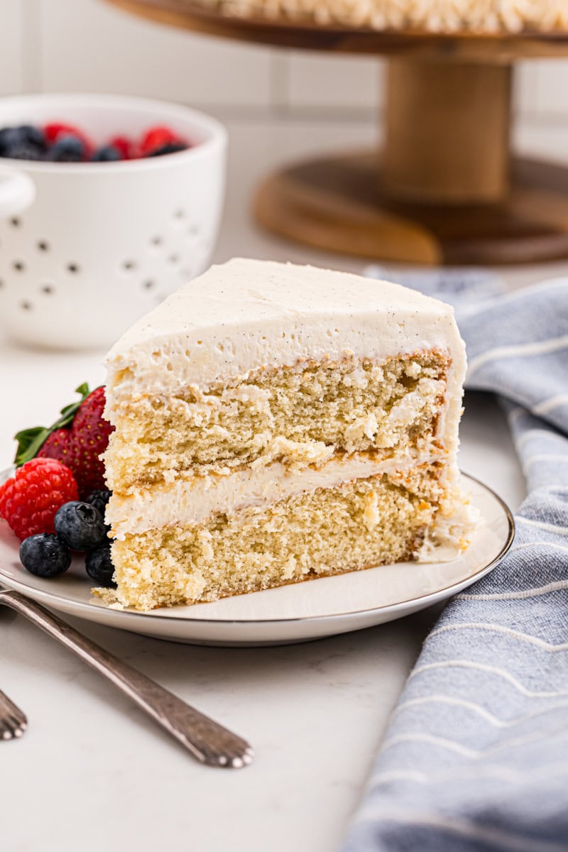 a slice of frosted vanilla layer cake served with fresh berries