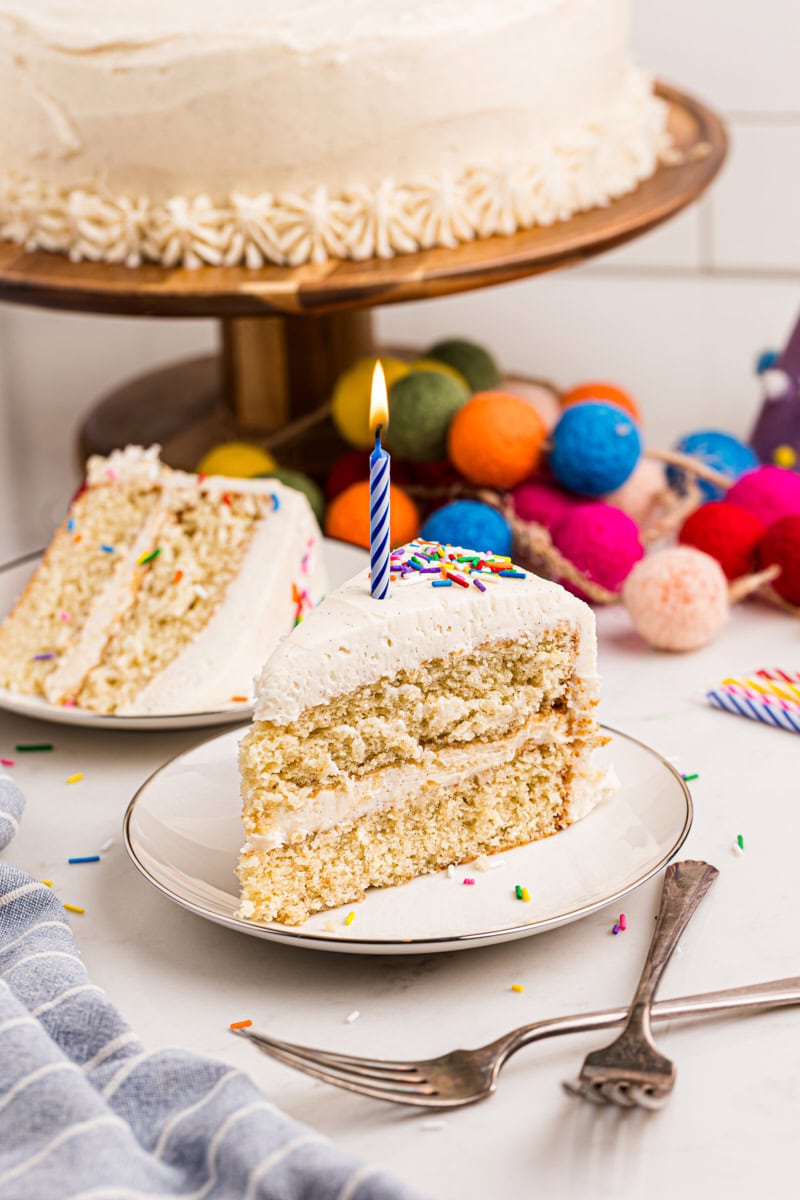 vanilla layer cake topped with fluffy vanilla buttercream, sprinkles, and a lit birthday candle