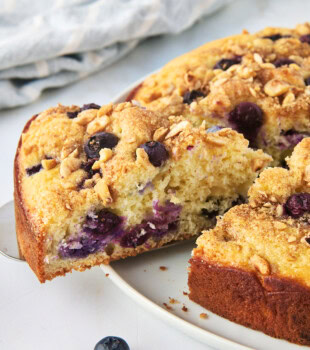 a slice of blueberry coffee cake on a cake server being removed from the remaining cake