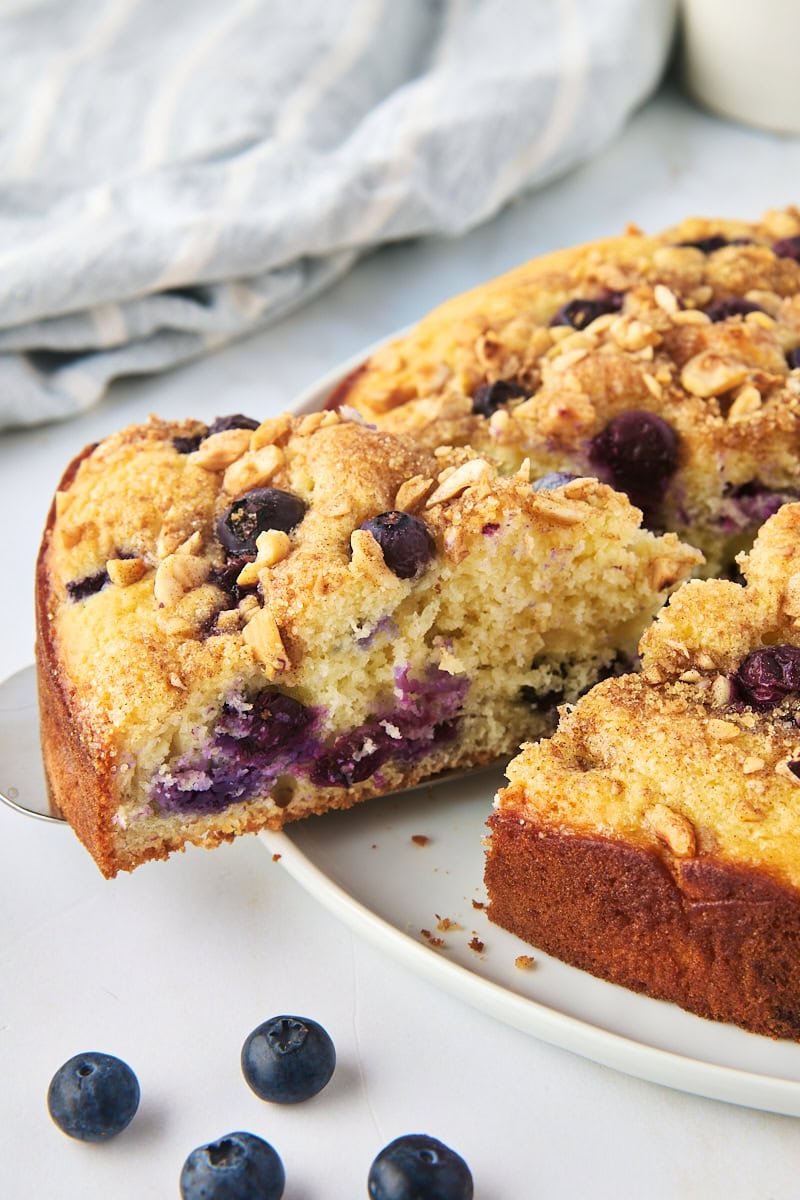 a slice of blueberry coffee cake on a cake server being removed from the remaining cake