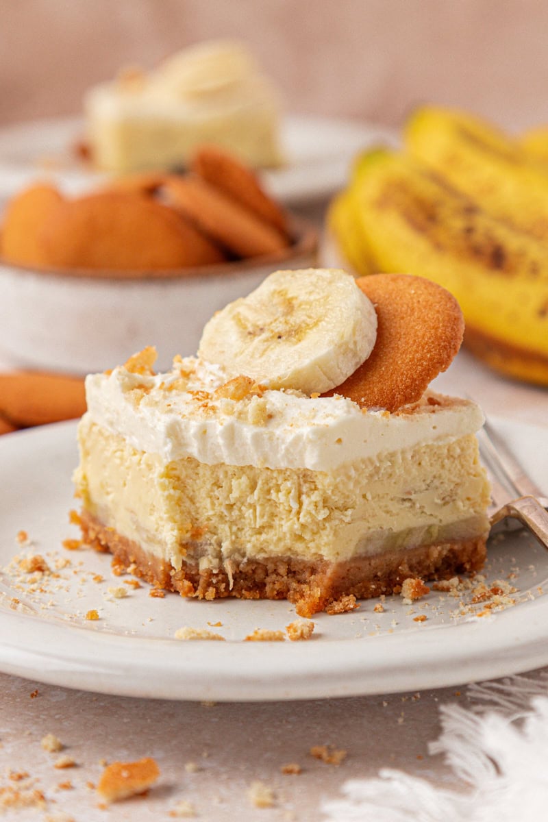 a banana pudding cheesecake bar featuring layers of vanilla wafer crust, creamy banana cheesecake filling, and whipped cream