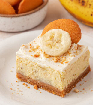 a banana pudding cheesecake bar topped with whipped cream, cookie crumbs, and fresh banana slice