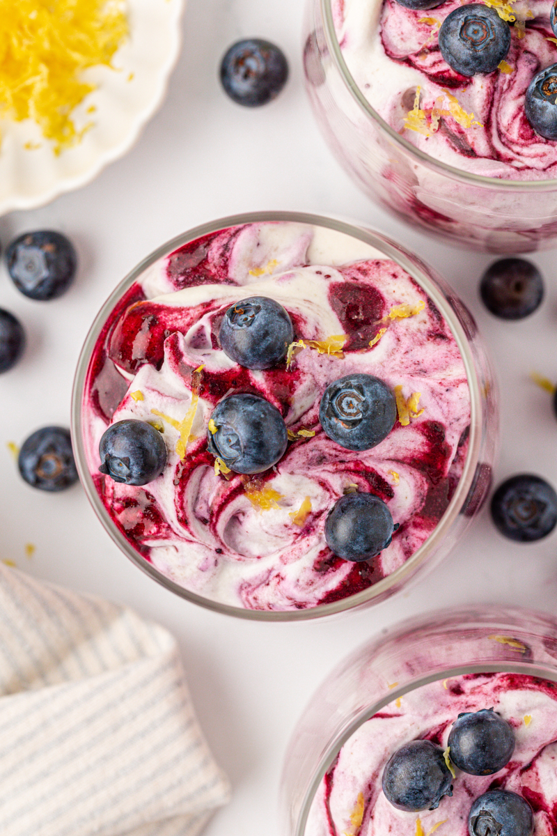 overhead view of swirled blueberry fool in a glass topped with fresh blueberries and lemon zest