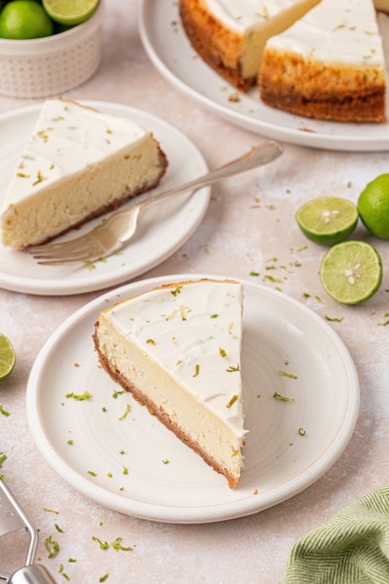 slices of Key lime cheesecake on plates with more cheesecake and limes in the background