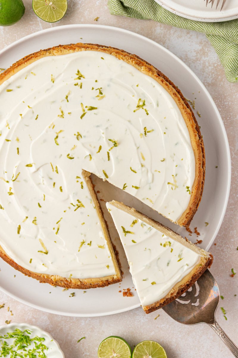 partially sliced Key lime cheesecake with sour cream topping and a sprinkle of lime zest