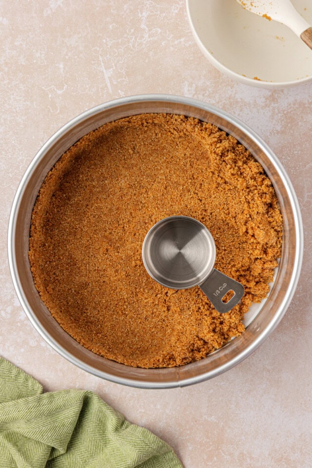 graham cracker crust mixture being pressed into a springform pan