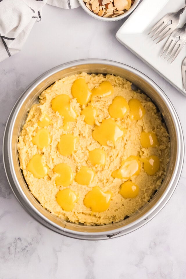 overhead view of lemon curd spooned on top of almond cake batter in a a cake pan