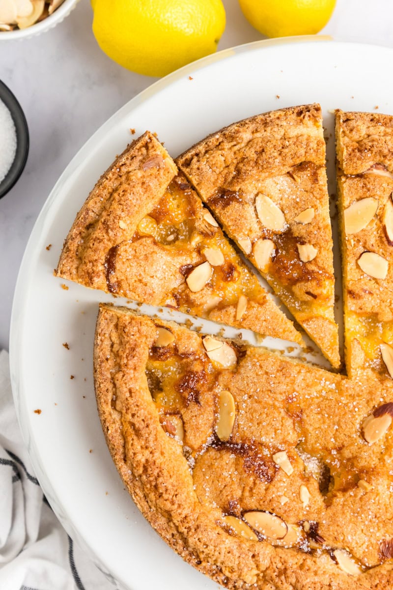 overhead view of partially sliced lemon almond cake with pockets of lemon curd and sliced almonds on top