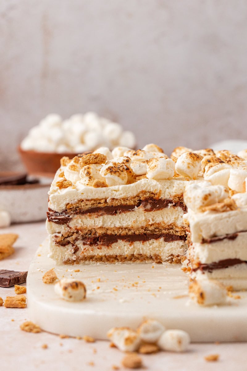 partially sliced s'mores icebox cake with layers of marshmallow filling, chocolate ganache, and graham crackers