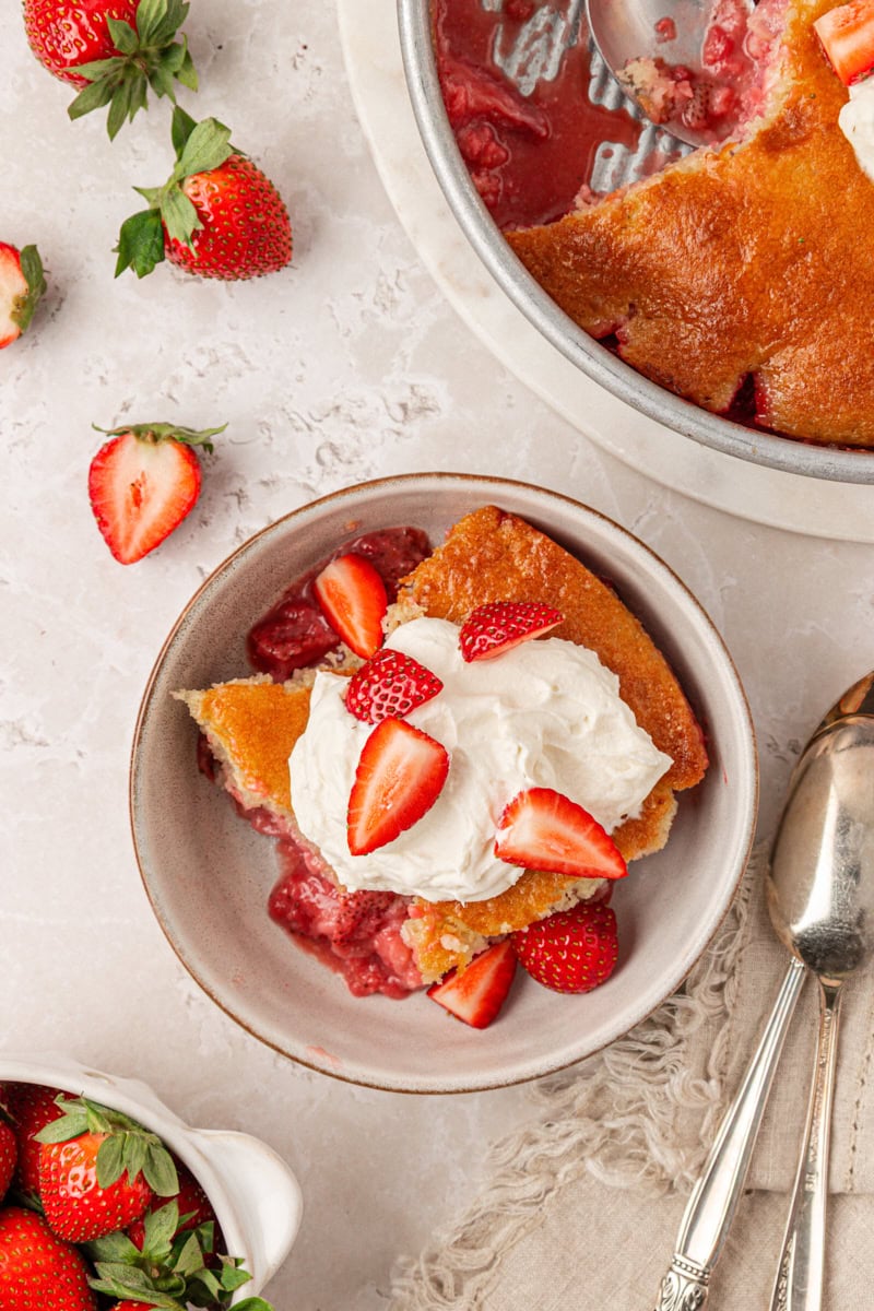 overhead view of a serving of strawberry spoon cake topped with whipped cream and fresh strawberries