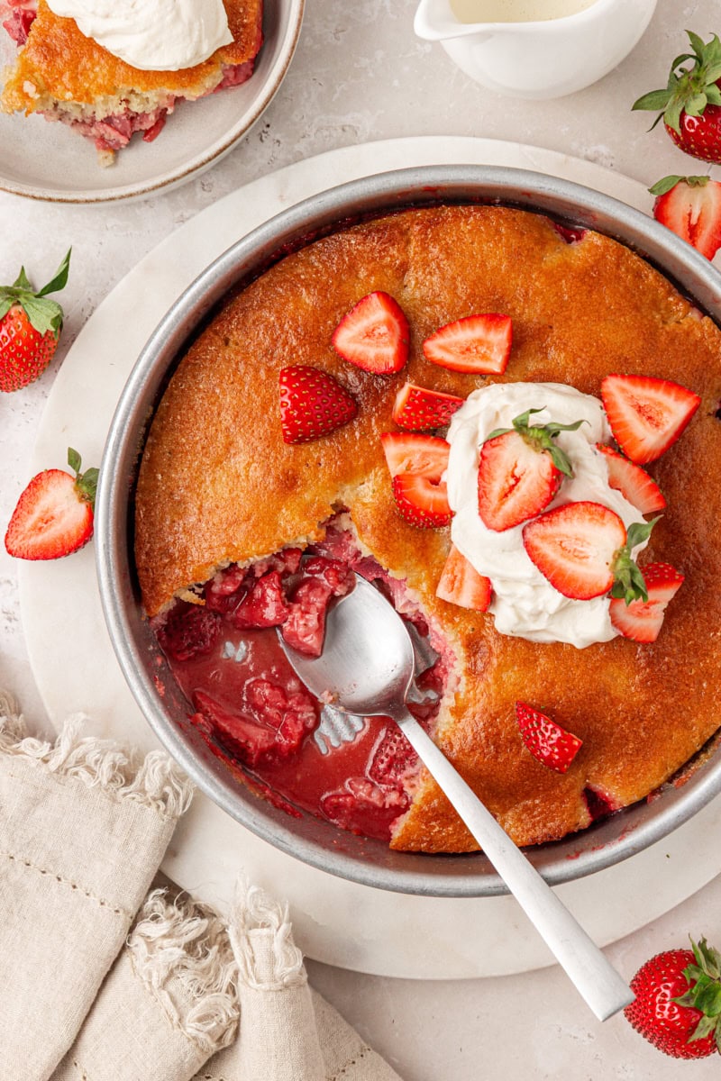 overhead view of strawberry spoon cake with a serving removed to show the berry filling underneath soft cake