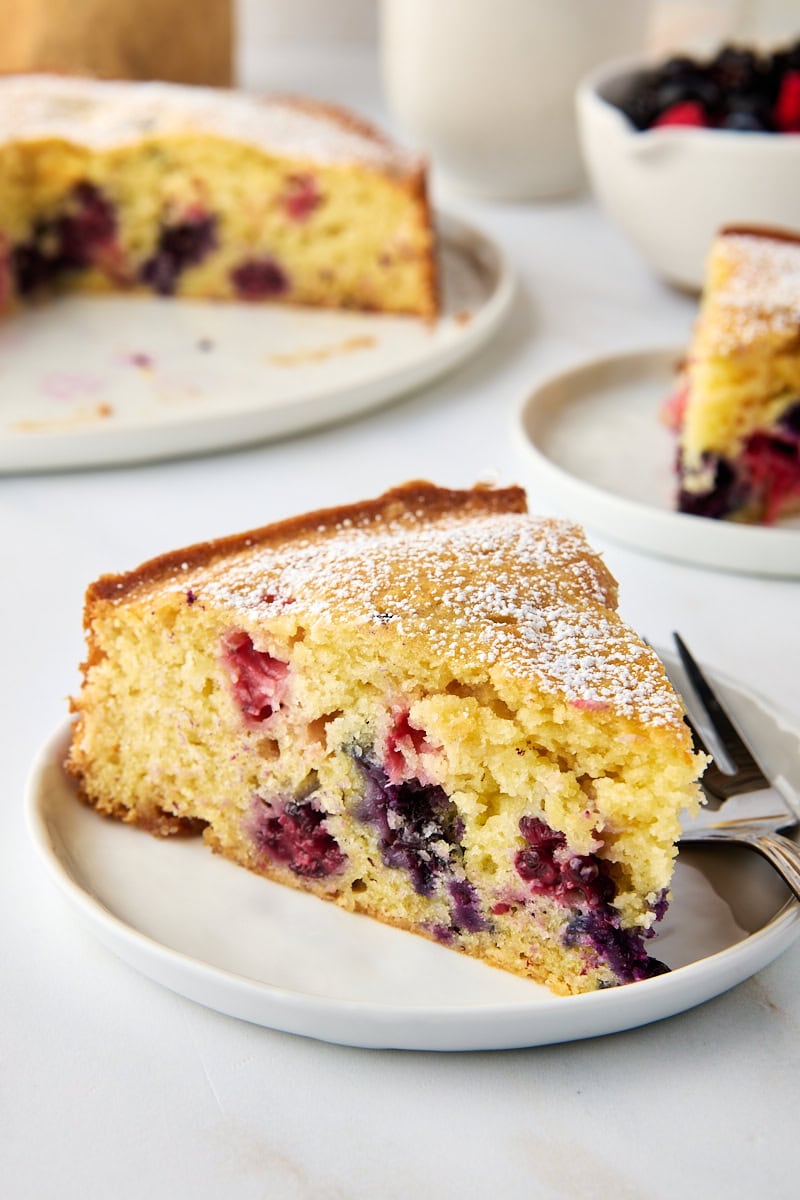 a slice of berry muffin cake filled with a mix of fresh berries and topped with a sprinkling of confectioners' sugar
