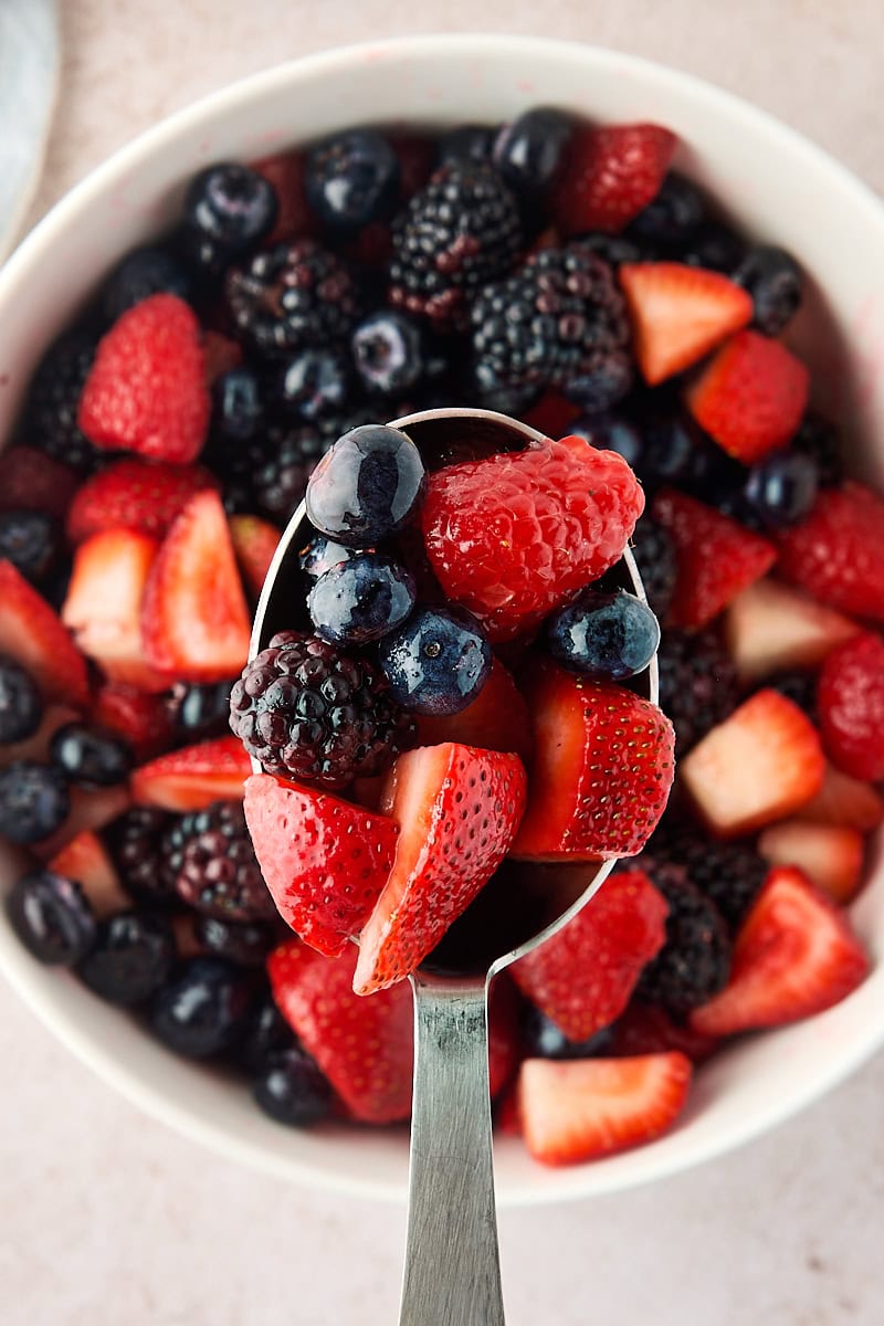 macerated berries in a serving spoon held over more berries in a bowl