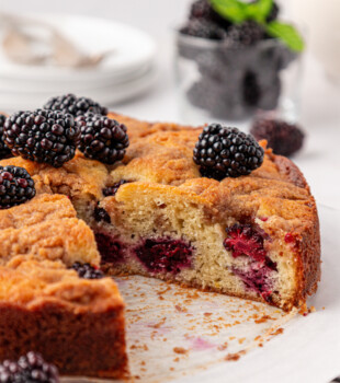 partially sliced blackberry buckle with fresh berries and a chunky crumb topping