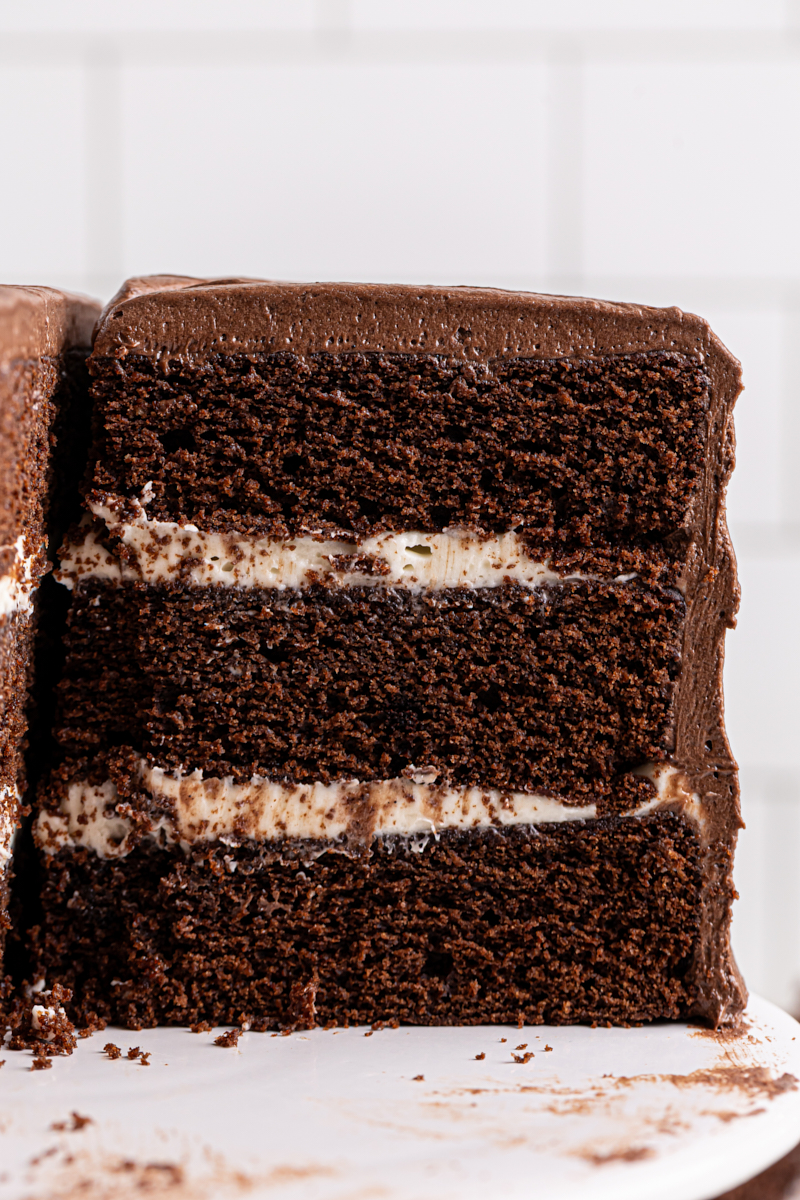 partially sliced chocolate cake with three layers of soft cake sandwiched around a tangy cream cheese filling and frosted with chocolate sour cream frosting