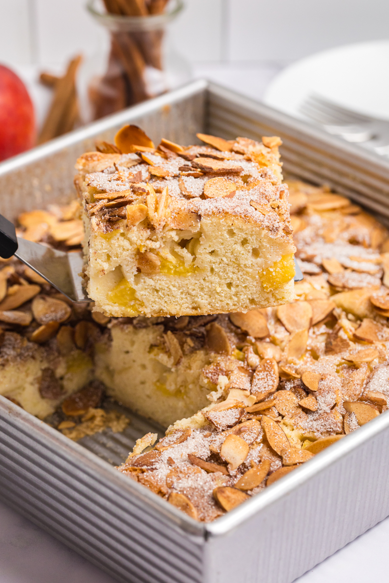 a slice of peach buckle on a cake server lifting away from the remaining buckle