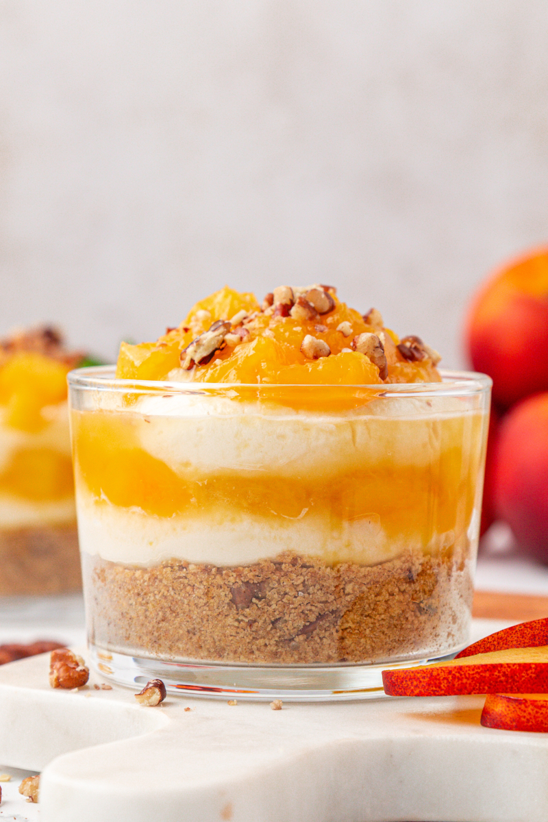 close-up of a peach cheesecake jar with layers of cookie crust, cheesecake filling, and peach compote