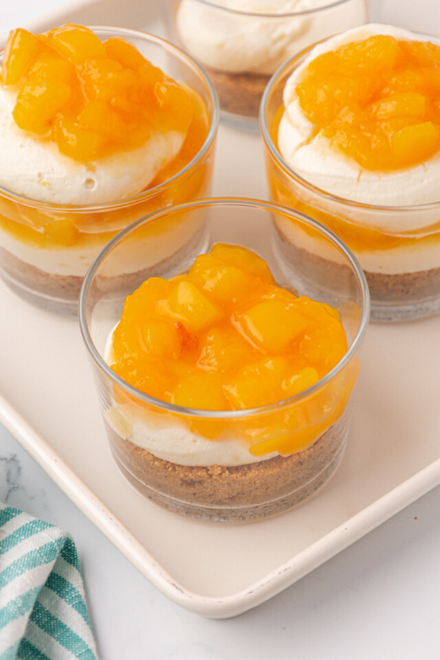 peach compote spooned over no-bake cheesecake filling and graham cracker crust in a dessert glass