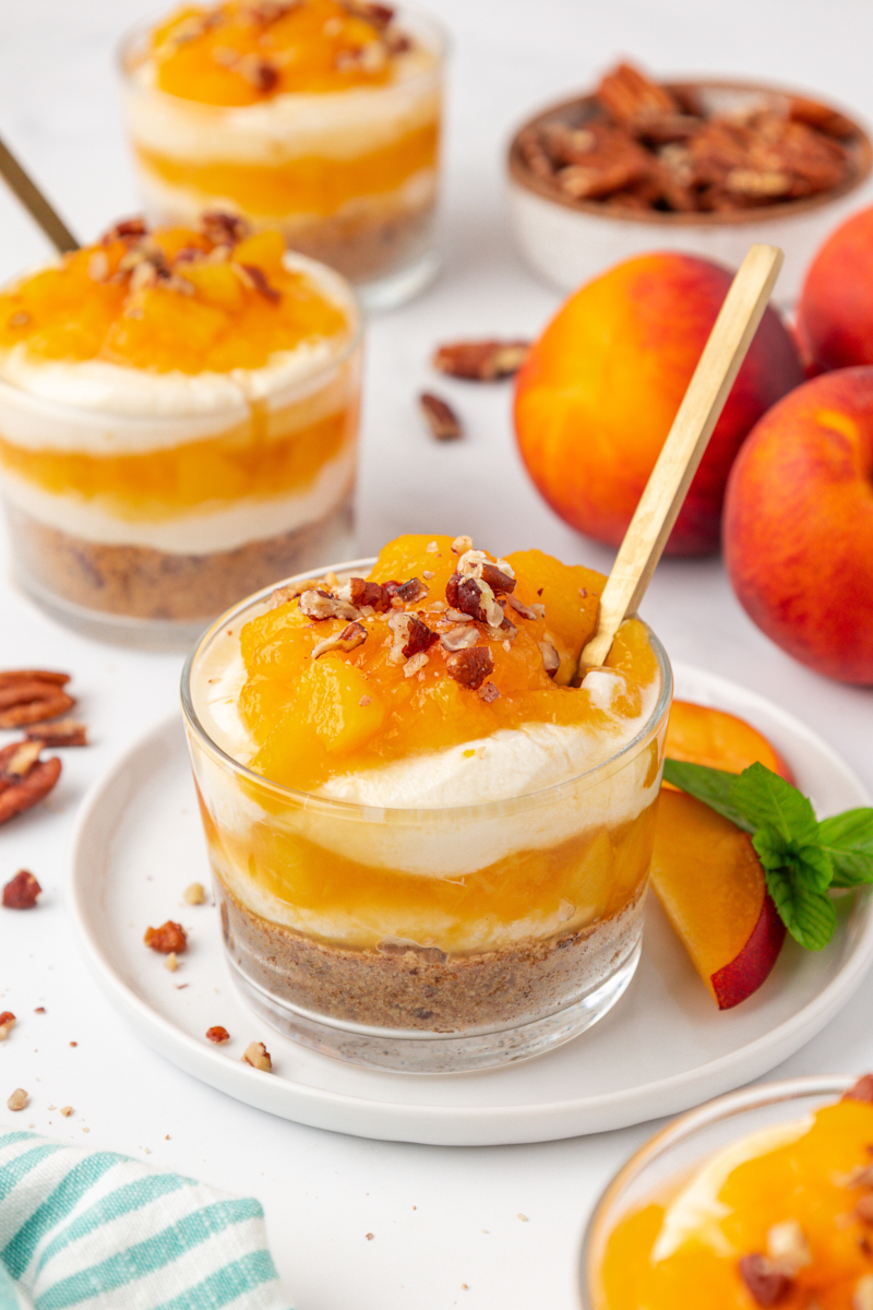 a no-bake peach cheesecake jar with nutty graham cracker crust, fluffy cheesecake filling, and fresh peach compote