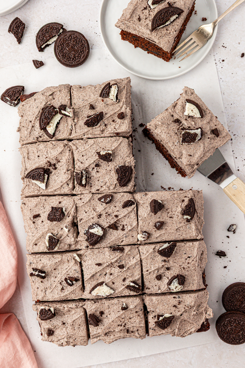 overhead view of sliced Oreo sheet cake topped with cookies and cream frosting and more cookie pieces
