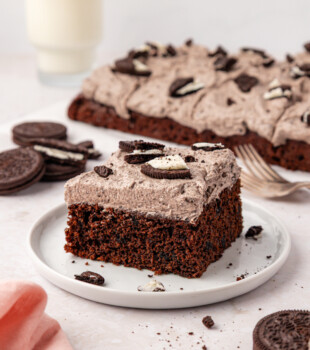 a slice of chocolate Oreo sheet cake on a white plate with the remaining cake in the background