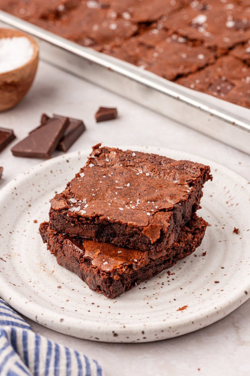 two stacked brownies on a plate with remaining brownies in a sheet pan in the background