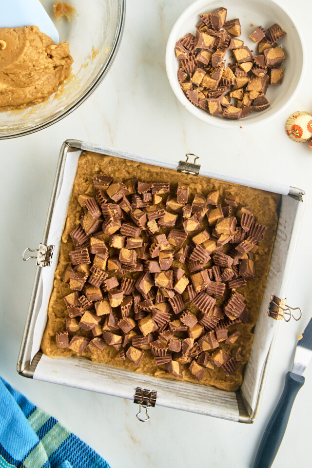 chopped peanut butter cups scattered on top of peanut butter blondie batter