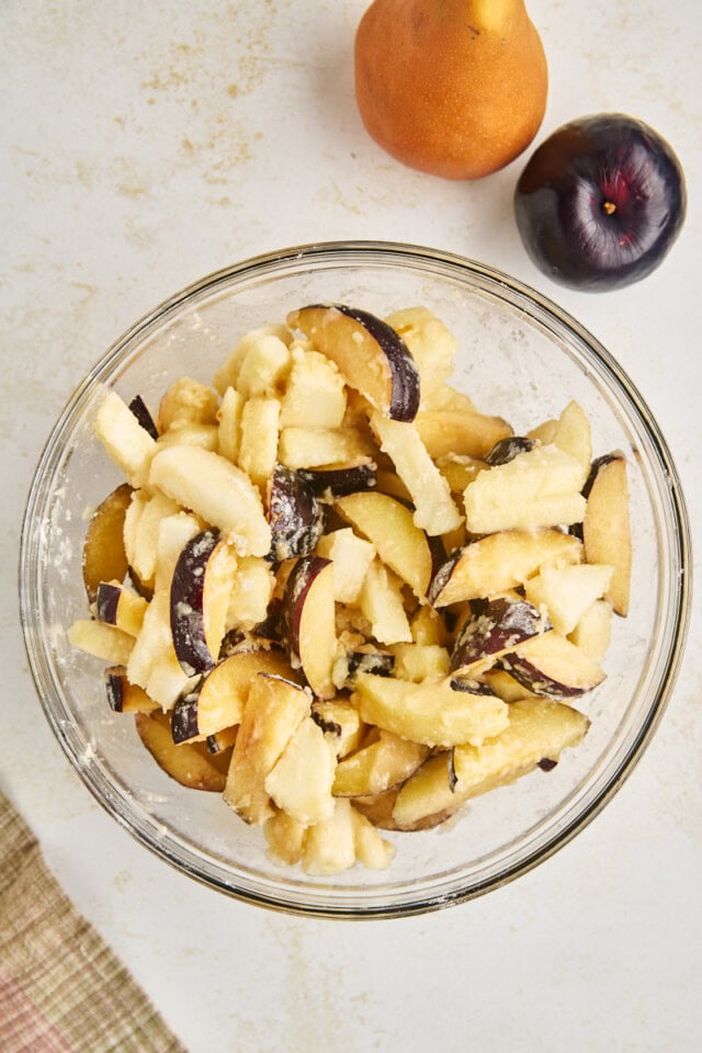 overhead view of sliced pears and plums tossed with flour mixture in a glass bowl
