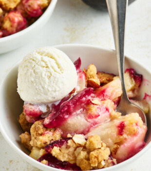 close up of a bowl of pear and plum crumble with cinnamon-almond topping, served with vanilla ice cream