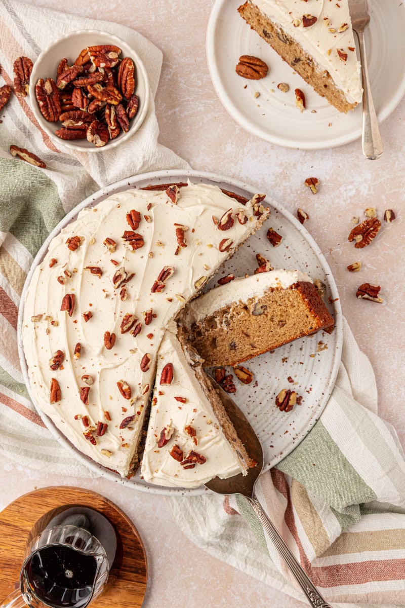 overhead view of a partially sliced single layer maple cake topped with maple frosting and toasted pecans