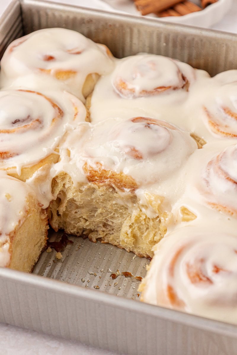 frosted cinnamon rolls in a metal baking pan with one roll missing