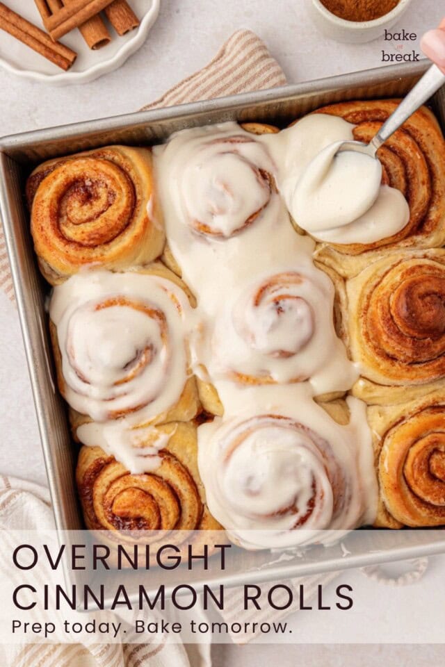 cream cheese frosting being spread over warm cinnamon rolls; text overlay "overnight cinnamon rolls - Prep today. Bake tomorrow."