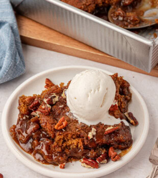 butterscotch pudding cake on a white plate with a scoop of vanilla ice cream and toasted pecans