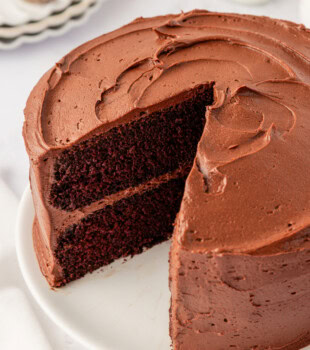 partially sliced two-layer devil's food cake with chocolate buttercream frosting