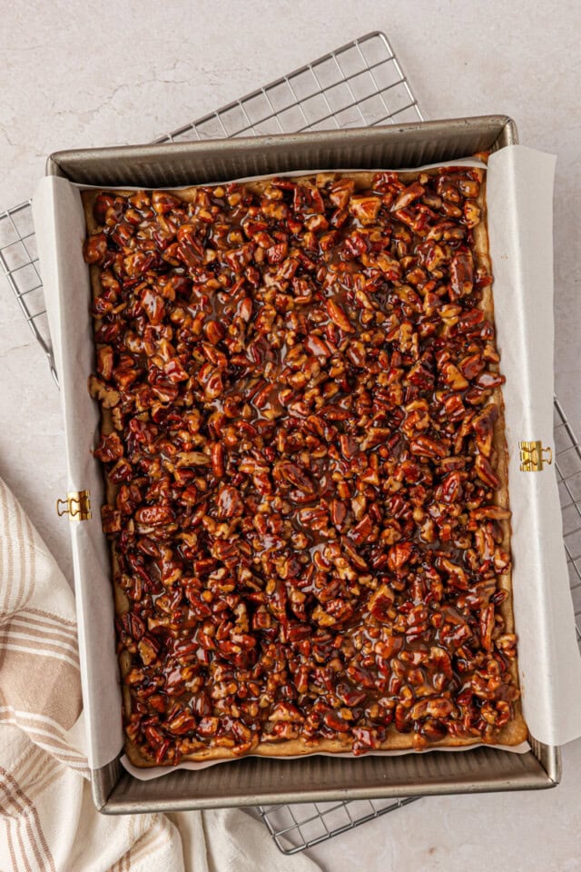 gooey pecan pie topping spread over cheesecake bars in a 9x13 pan