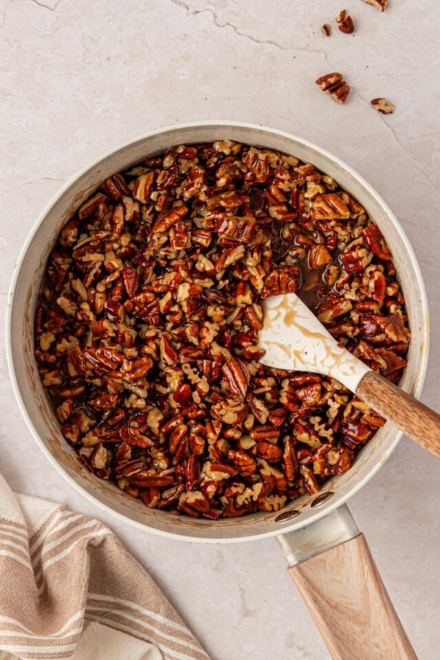 chopped pecans coated in glossy brown sugar caramel in a saucepan, with a spatula resting in the mixture