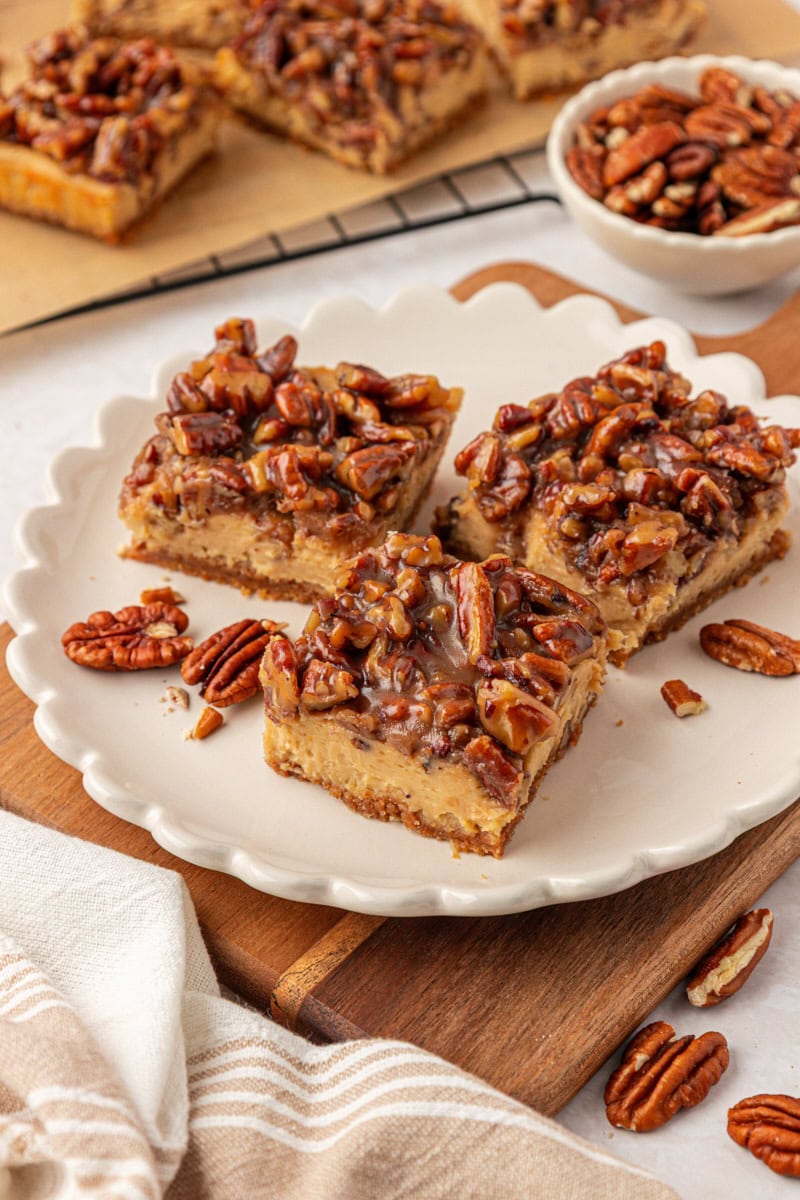 three pecan pie cheesecake bars on a white plate